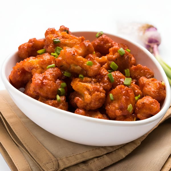 A white bowl filled with Desi Chowrastha's Gobi Manchurian, garnished with chopped green onions.