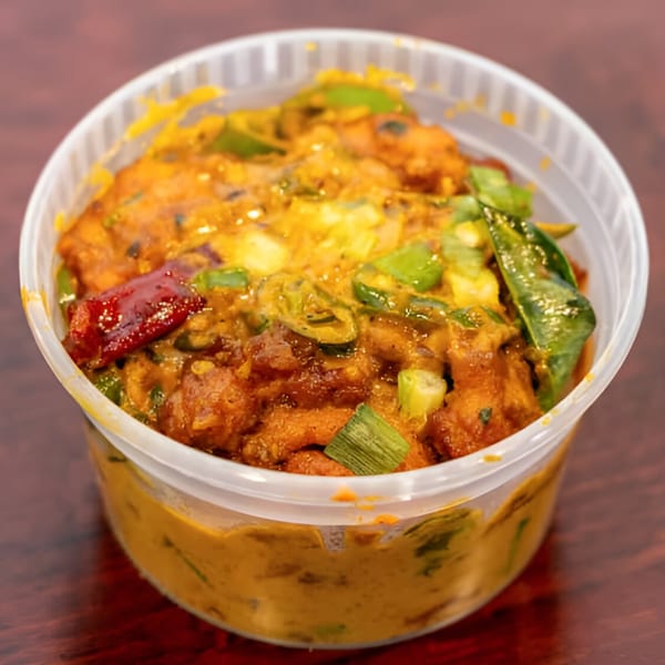 Indian chicken dish with green peppers, red chilies, and curry leaves in a clear plastic container.