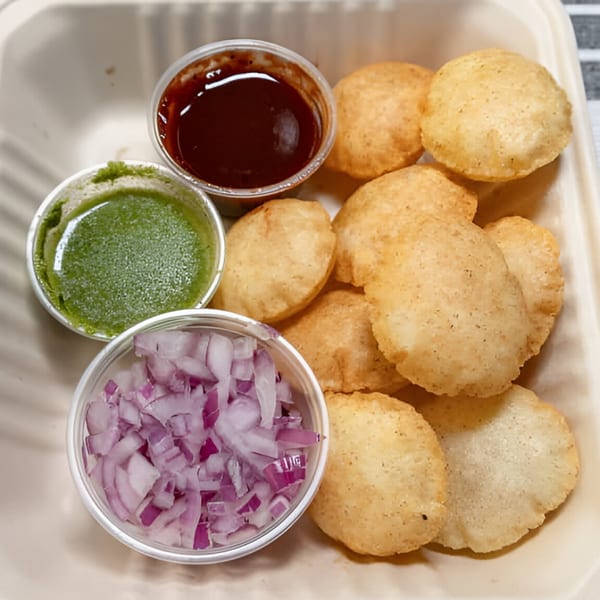 Pani Puri with three small cups of sauces and chopped red onions in a white container.