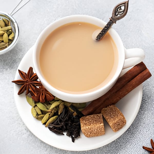 A white cup of Indian chai tea with a decorative spoon, surrounded by spices like star anise and cardamom.