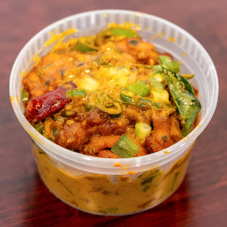 Desi Chowrastha's Indian dish in a clear plastic container, garnished with green onions and red chili.