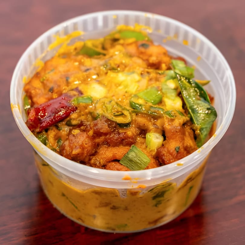 Desi Chowrastha's Indian dish in a clear plastic container, garnished with green onions and red chili.