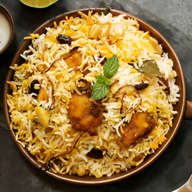 A close-up of Desi Chowrastha's chicken biryani, garnished with mint, cashews, and raisins.