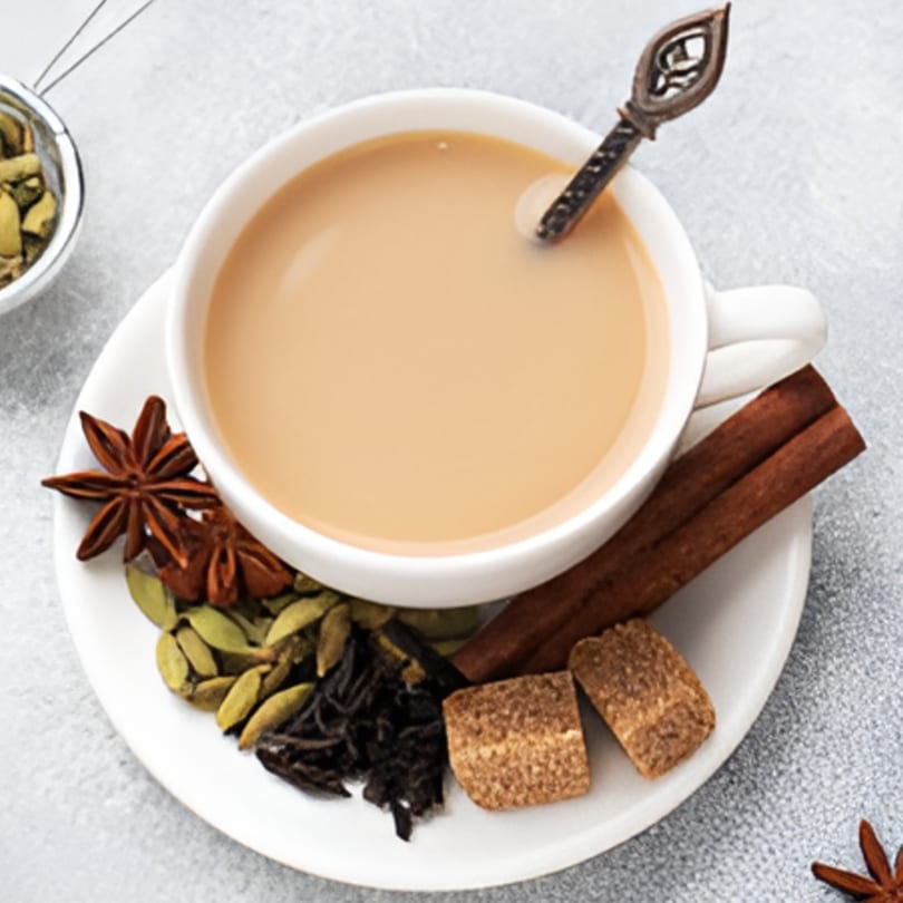 A cup of Indian chai tea with star anise, cardamom pods, cinnamon sticks, and brown sugar cubes.